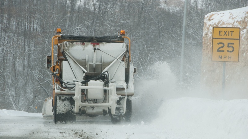 Snow plow plowing near speed limit sign