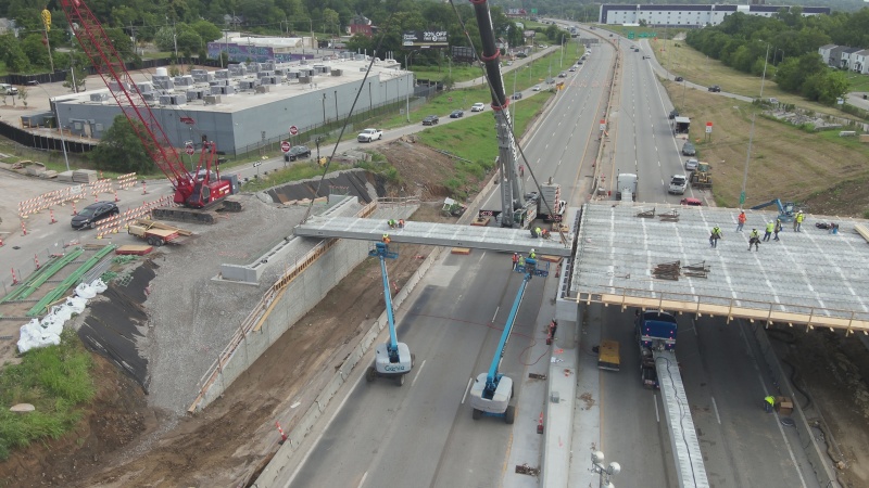 Crane and crews installing a girder on a new bridge over a closed highway